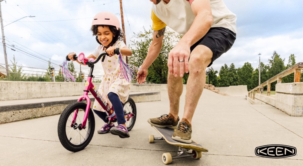 A girl riding her bike with her dad skateboarding 