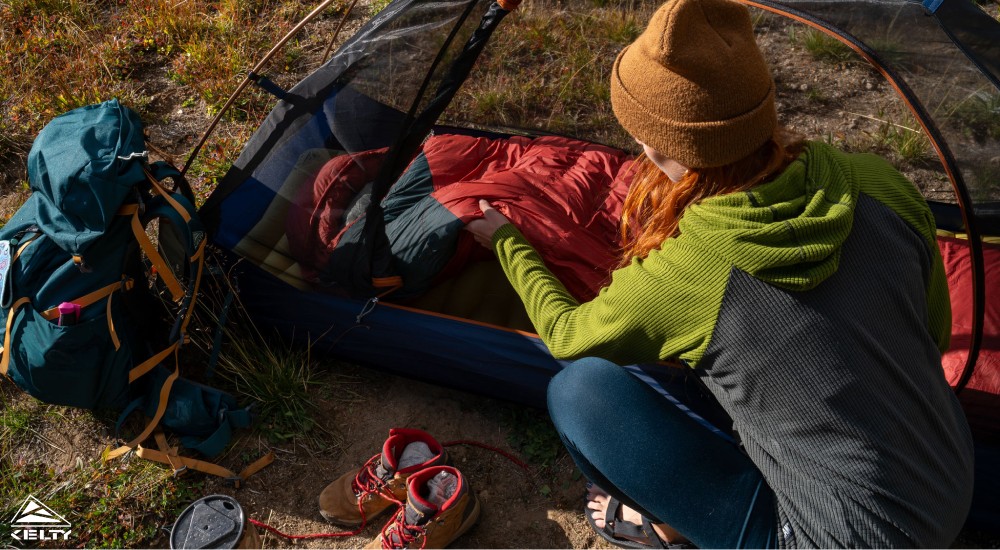 a woman laying out her sleeping bag in a tent