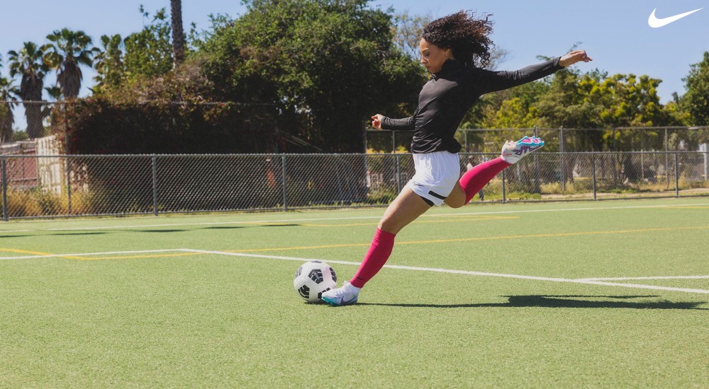 a girl kicking a soccer ball while wearing nike soccer cleats