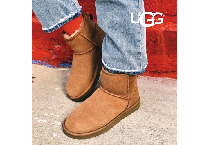 Woman standing against a bright red brick wall wearing brown UGG Classic Mini boots