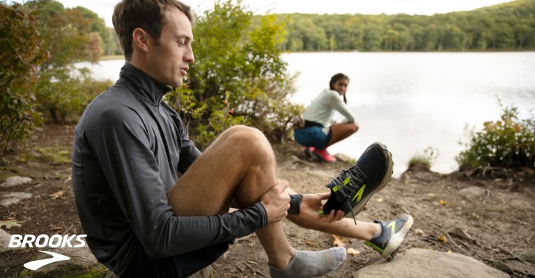 a man putting on his running shoe next to water
