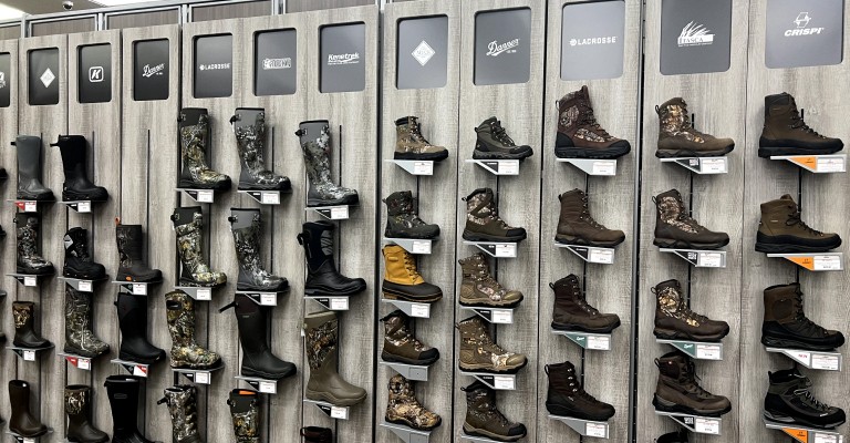 a variety of hunting boots on a wall within the hunting shop