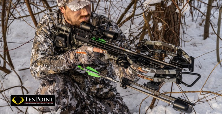 Hunter holding a crossbow in a snowy wooded area on the hunt