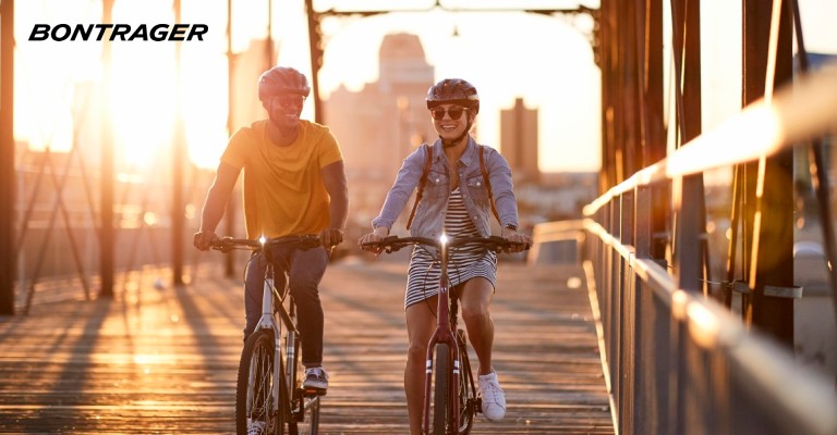 Two people use bike lights while riding near sunset