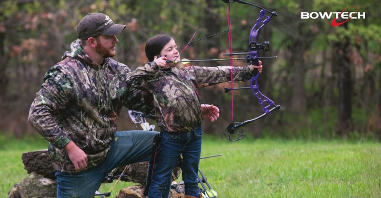 Youth hunter shooting a compound bow with an adult