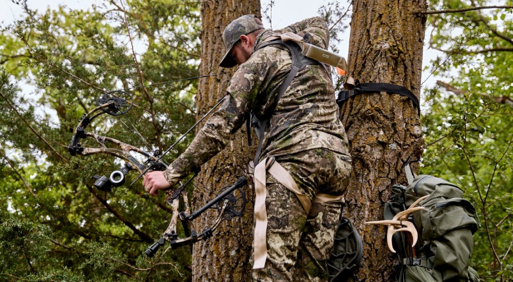 a hunter pulling a bow back in a treestand