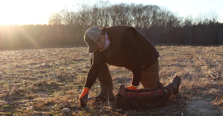 alan, a hunter, setting a trap in a field