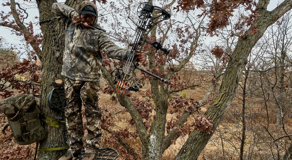 a hunter using a compound bow on a treestand