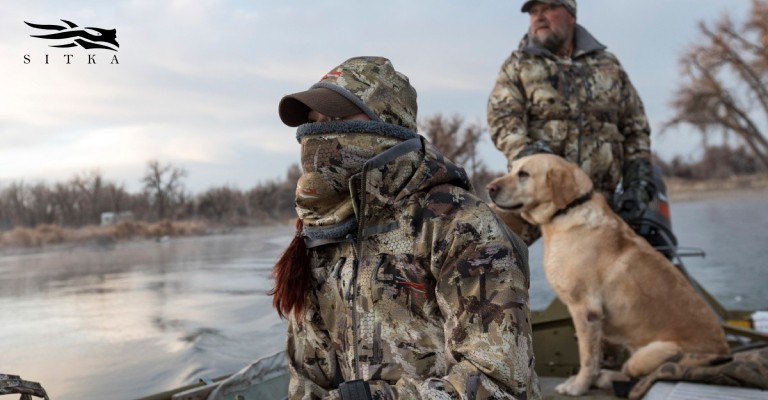 duck hunters in duck hunting clothing on a boat with a hunting dog