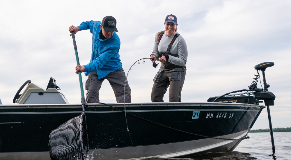 two people on a boat reeling in a fish