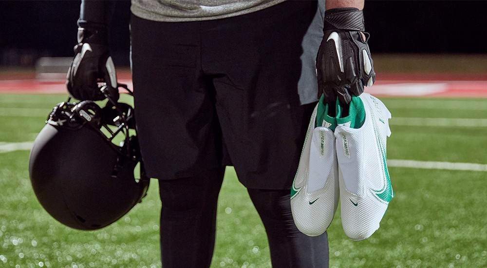 football player wearing football gloves and holding a helmet and cleats