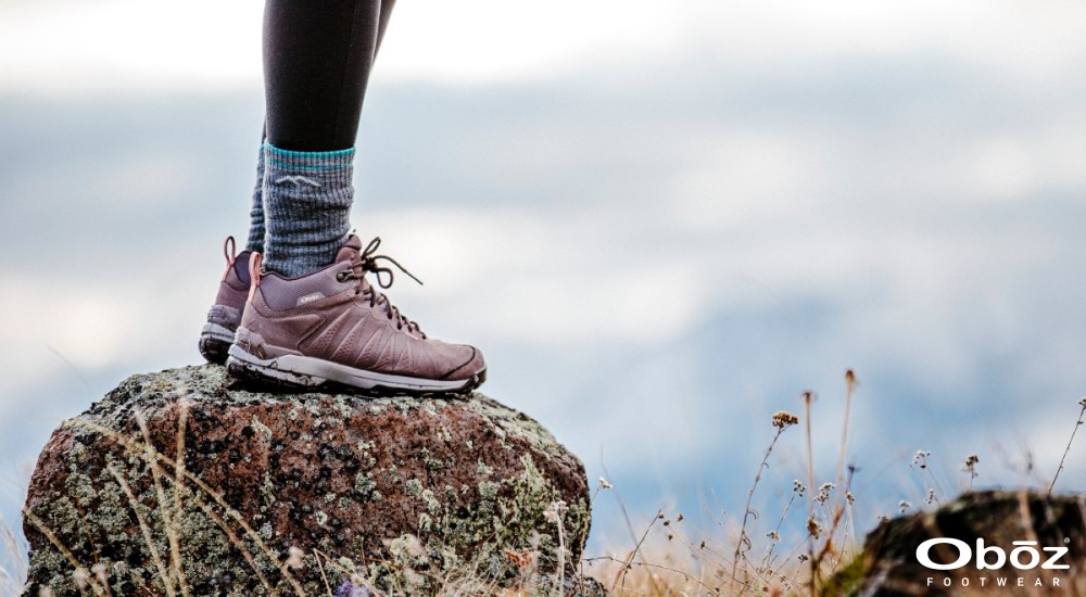 a woman standing on a rock wearing hiking boots