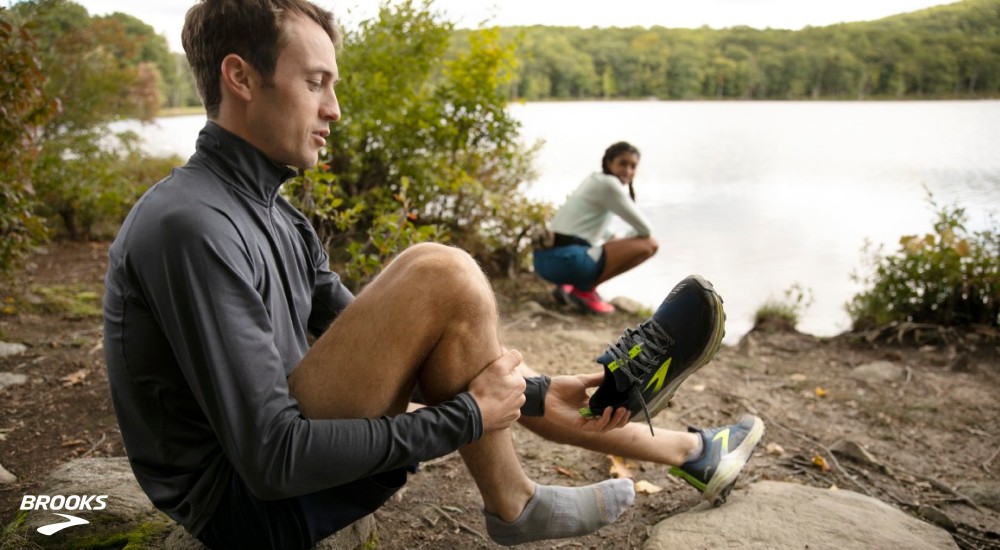 a runner putting on his running footbed shoes next to a lake