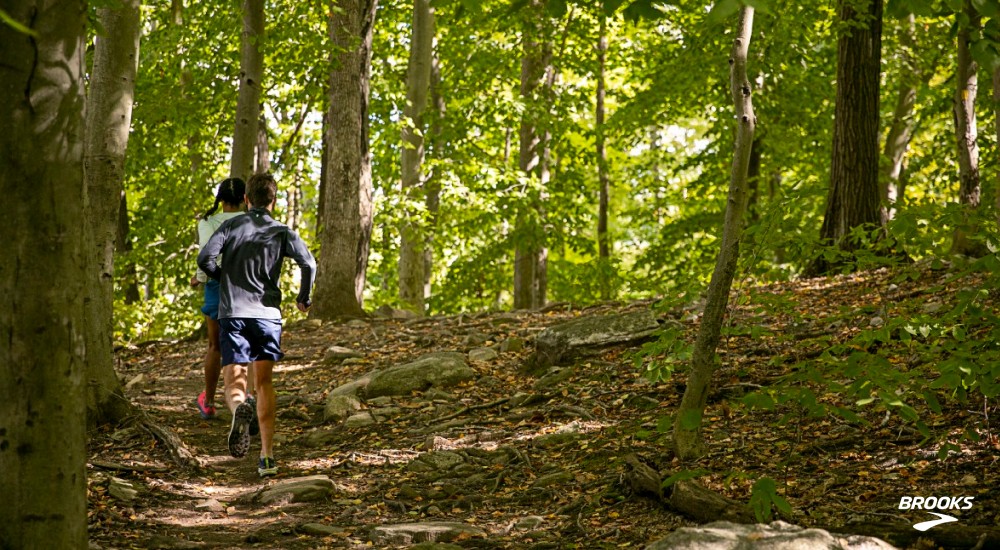 two people running through the woods on a trail
