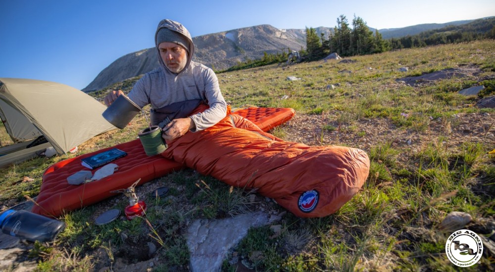 a man drinking coffee while in a sleeping bag out backpacking