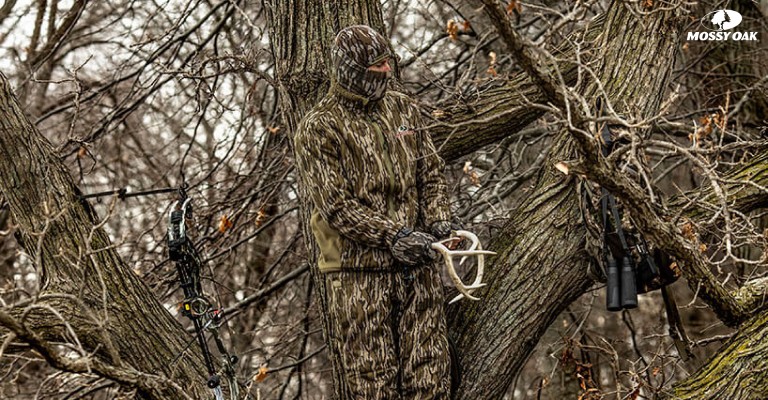 a hunter in a tree wearing mossy oak bottomland