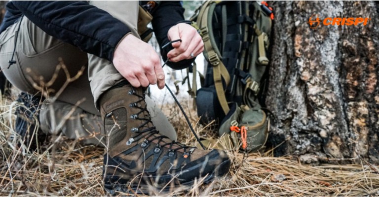 man lacing up his crispi boots in the woods