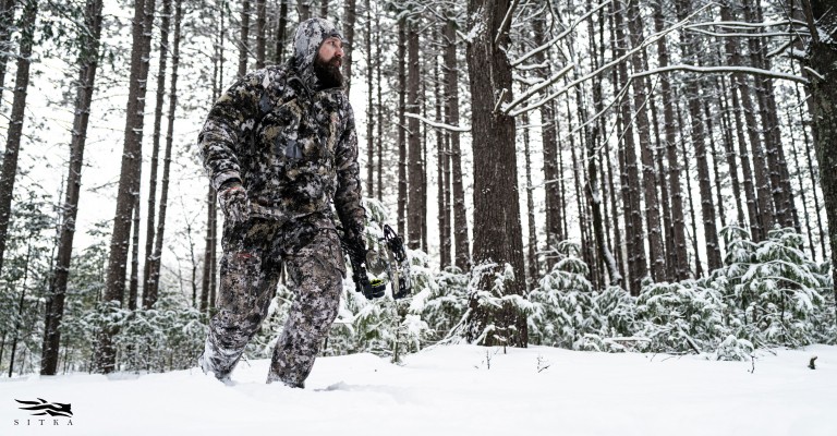 a hunter walking through the snow wearing stika elevated ii