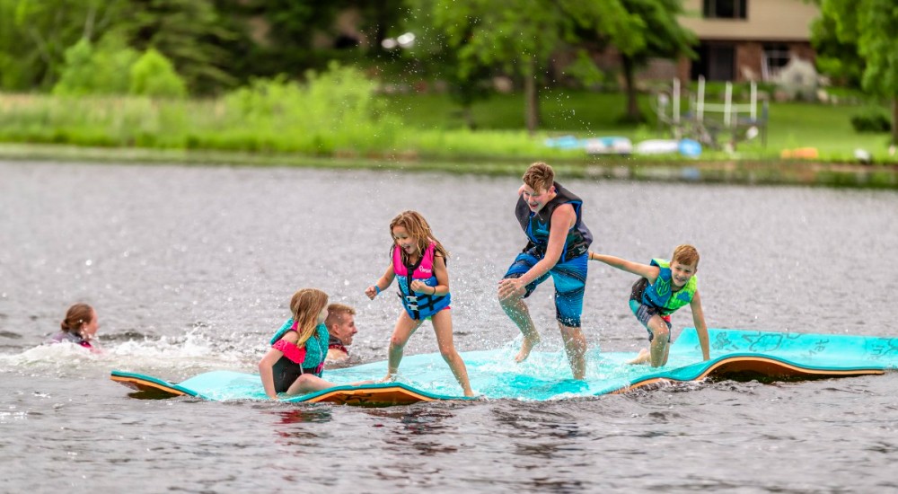 a family on an aqua lily pad wearing bright color swimsuits