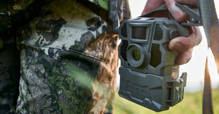 a hunter holding a trail camera in the field